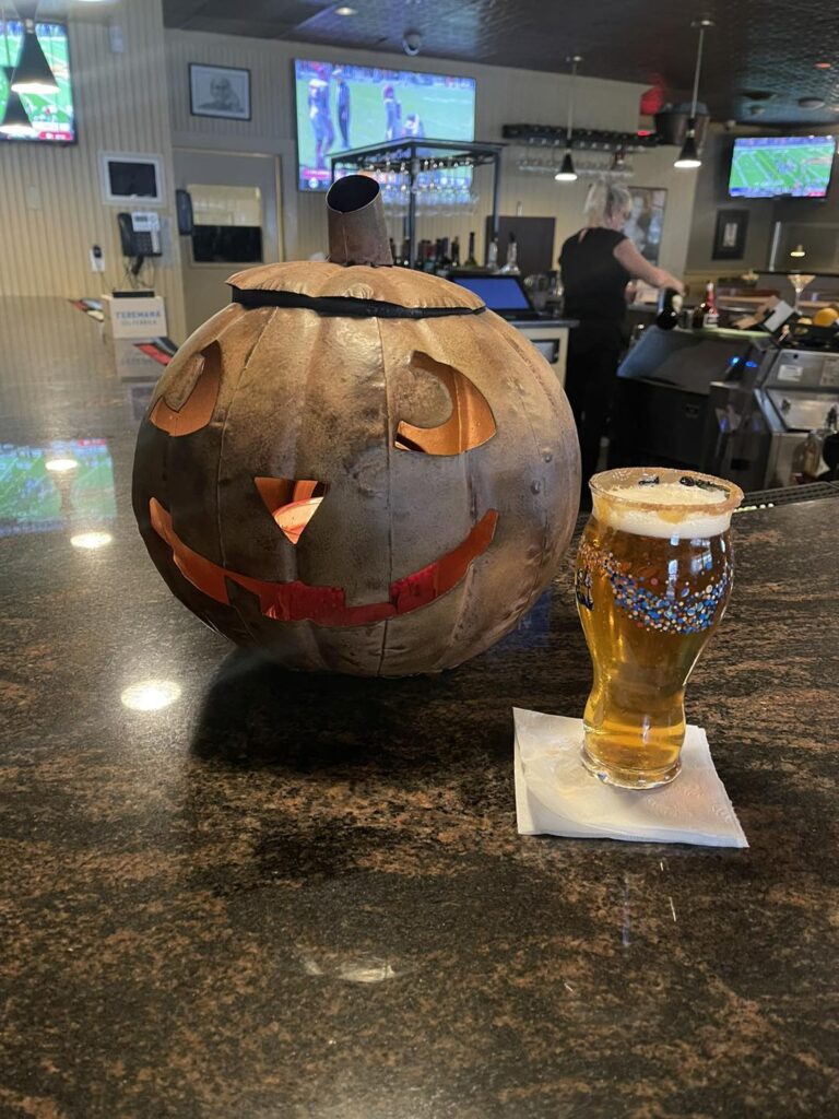 A carved pumpkin and a cold draft beer on the bar