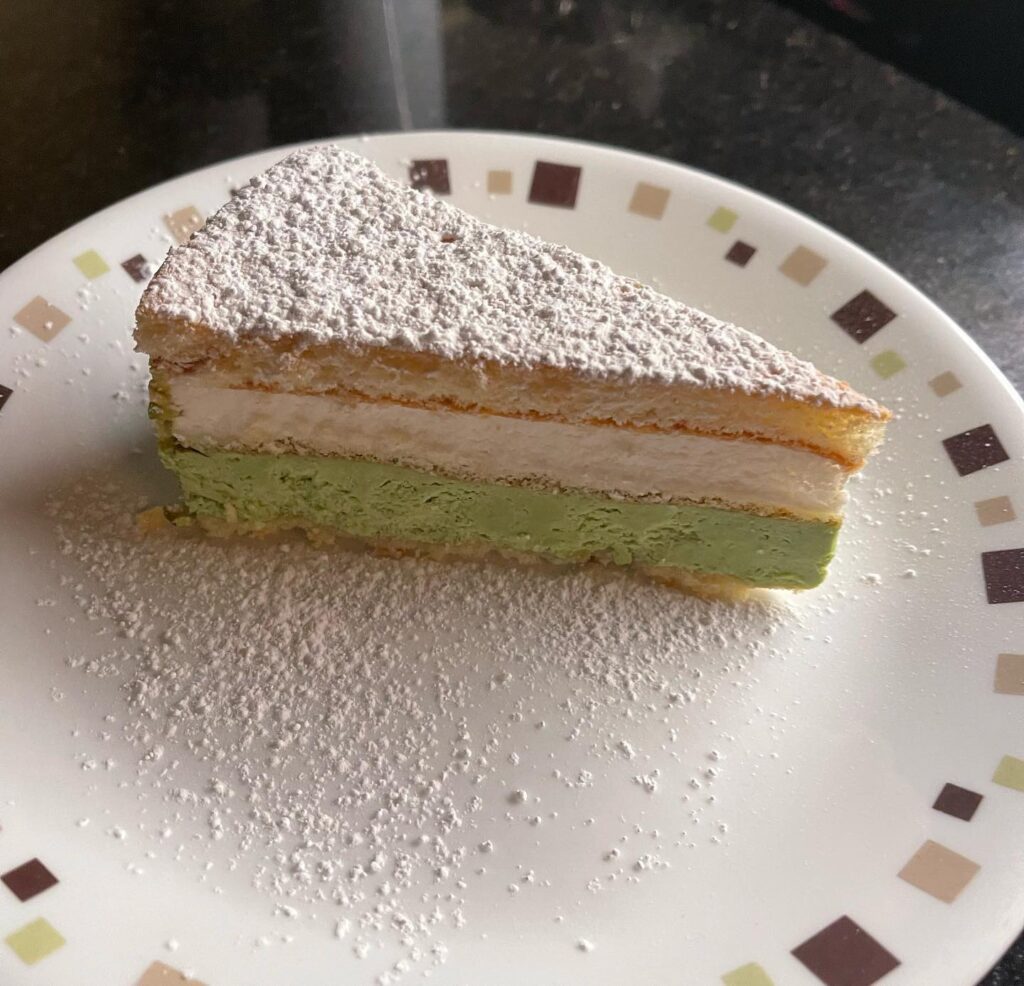 Slice of pistachio and cream layer cake dusted with powdered sugar